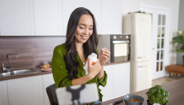 woman-reading-vitamin-bottle-in-kitchen-600x344.jpg